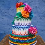A beautiful Quinceanera cake with buttercream frosting. The cake is multicolored with vibrant flowers on top.