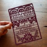A person holding a purple paper cut out of paper featuring laser cutting graphic design for a Quinceanera invitation.