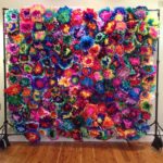 Quinceanera image: A large multicolored flower wall hanging on a wall with Mexican flowers
