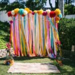 A Quinceanera in a Mexican backyard with a beautiful arch adorned with colorful ribbons and pom poms.