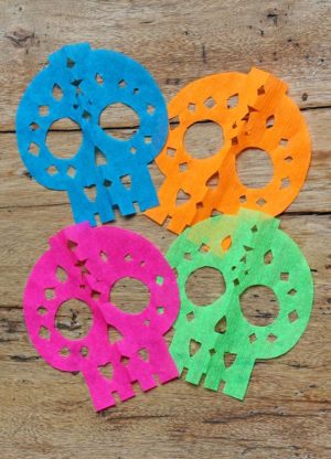 Paper papel picado de calavera with four sugar skulls on a wooden table for Quinceanera