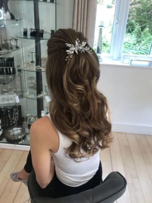 A woman with a half up half down hairstyle with accessories, sitting in a chair with a hair comb in her hair for a Quinceanera celebration