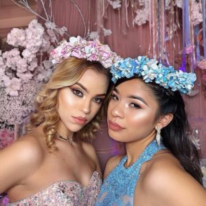 Two beautiful young women posing for a picture, surrounded by flowers in a Quinceanera celebration