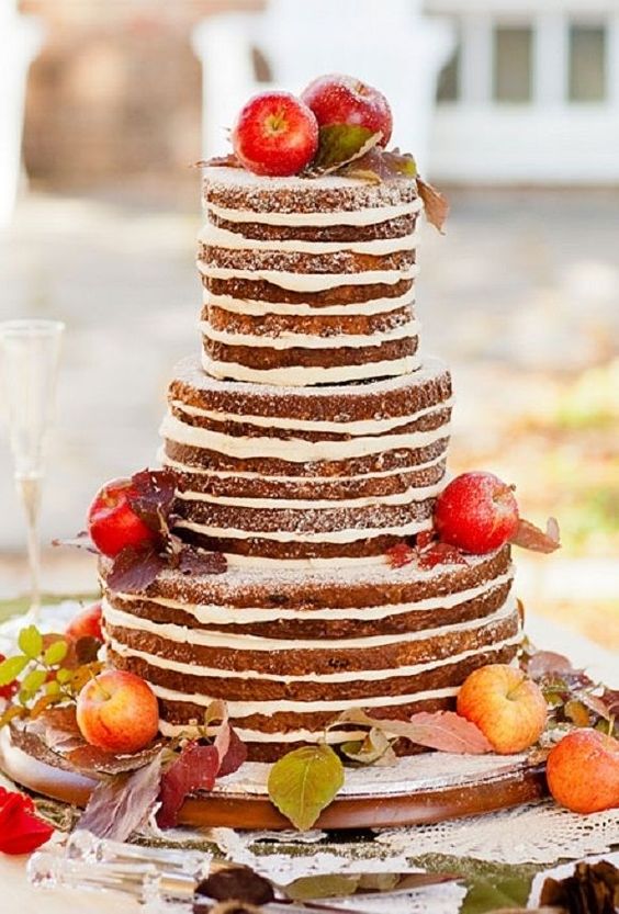 A quinceanera centerpiece depicting a three tiered cake with fruit on top of it surrounded by apples.