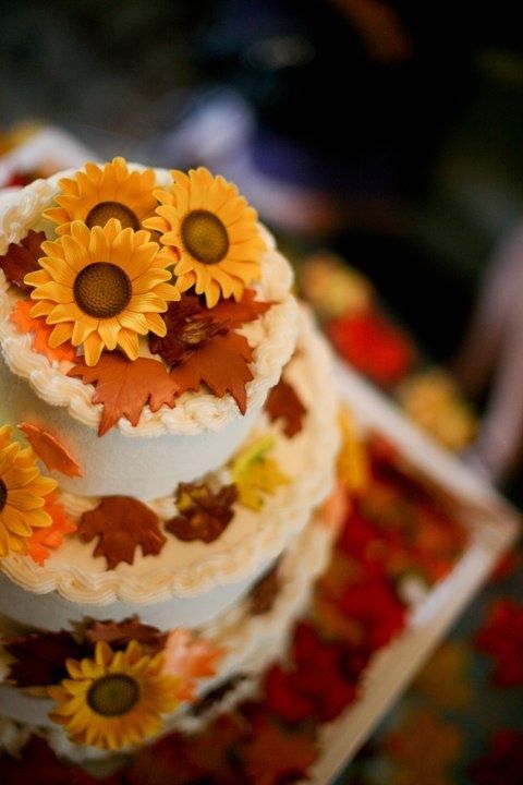 A three-tiered Quinceanera cake decorated with sunflowers and leaves, perfect for a fall-themed celebration.
