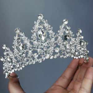 A hand holding a tiara with a diamond crown on it, suitable for a Quinceanera celebration