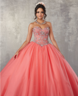 A woman in a coral Quinceañera dress posing for a picture in a ball gown