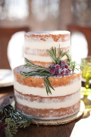A beautiful three-tiered Quinceanera cake with frozen dessert icing, adorned with berries and greenery on top.