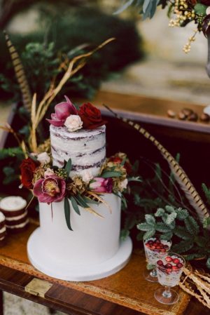 Quinceanera image description: A navy blue rustic wedding invitation accompanied by a white cake adorned with flowers and greenery on a table.