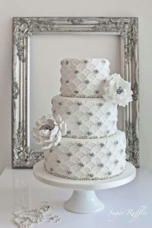 Elegant silver Quinceanera cake, a white cake with silver decorations sitting on top of a table