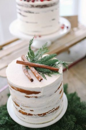 A rustic winter Quinceanera cake with icing, featuring a white cake topped with cinnamon sticks.