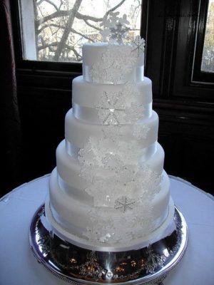 A white Quinceanera cake sitting on top of a table with an elegant winter theme