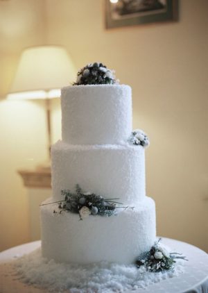 A three-tiered white Quinceanera cake with pine cones on top and snow-like icing