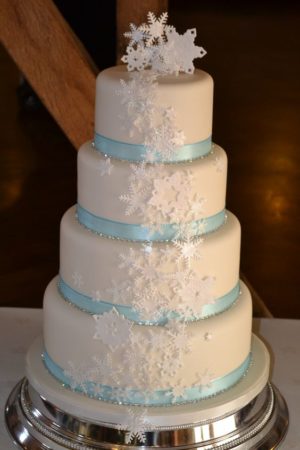 A Quinceanera cake with cascading snowflakes on top, surrounded by cupcakes