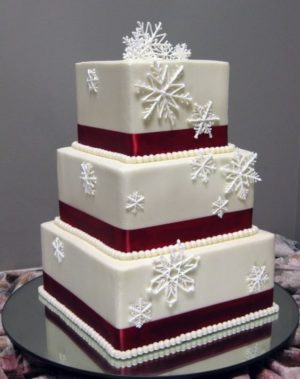 A three tiered Quinceanera cake decorated in red, white, and silver, with snowflakes on top.