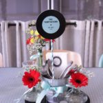A Quinceanera celebration with a rock and roll theme, featuring a table adorned with a vase filled with red flowers.
