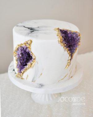 A Quinceanera géode cake with white base and purple and gold decorations on it