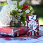Rockabilly Quinceanera decorations. A car, a vase with flowers, and a card on a table.