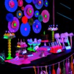 A table at a Quinceanera party topped with lots of different types of decorations and glow in the dark party ideas.