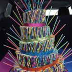 A multicolored Quinceañera cake with lots of sprinkles on it, featuring unique Quinceanera themes