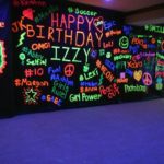 A glow in the dark Quinceañera with a blacklight. The venue features a black wall with neon writing on it.
