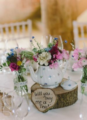 A Quinceanera-themed table with teapot centerpieces. The table is topped with vases filled with flowers.