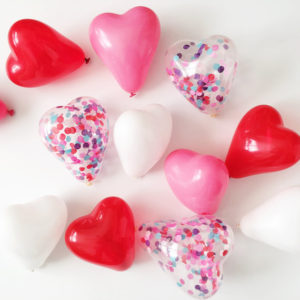 A Quinceanera-themed image featuring a heart-shaped balloon and a bunch of heart-shaped balloons with confetti sprinkles.