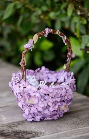 A lilac flower basket with purple flowers on a wooden table, perfect for a Quinceanera celebration