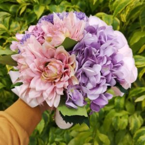 A person holding a bouquet of purple and pink flowers, with a floral design of cut flowers
