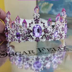 A Quinceanera crown jewellery with purple crystals on it, held by a person.