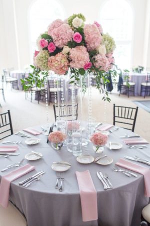 A baby pink and grey Quinceanera theme wedding invitation, featuring a table with a vase of flowers on top of it.