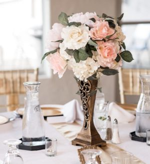 A Quinceanera image featuring rose gold and silver Quinceañera dresses, with a table displaying a vase of flowers on it.