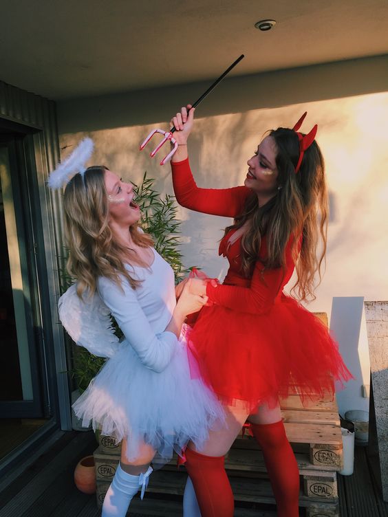 Two women dressed up as devil and angel in Quinceanera themed Halloween costumes, holding umbrellas