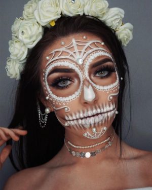 A woman wearing a white sugar skull makeup costume for a Quinceanera, known as maquillaje de catrina blanco.
