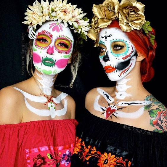 Two women with face paint and flowers on their heads, showcasing a Quinceanera makeup look inspired by the catrina veracruzana