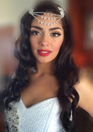 A woman with long, black hair wearing a white dress and a headpiece celebrating a Quinceañera.