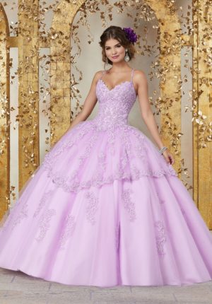 A woman in a size 0 Quinceanera dress standing in front of a gold wall, wearing a purple ball gown