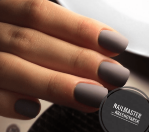 A person with a gray manicure on their hand holding a nail polish bottle