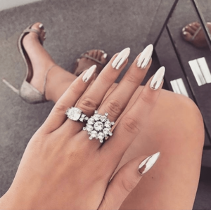 A woman with white nails showcasing intricate quinceanera-themed nail art, complemented by a delicate ring on her finger.