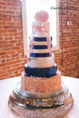 A simple navy and pink Quinceanera cake, featuring three tiers and a pink rose on top