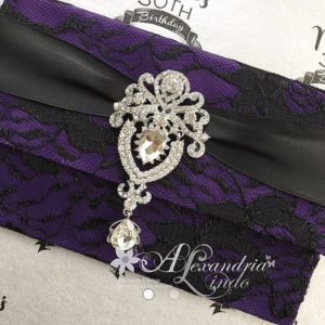 A Quinceanera-themed image featuring a magenta jewellery. The image showcases a purple and black invitation adorned with a broochet.