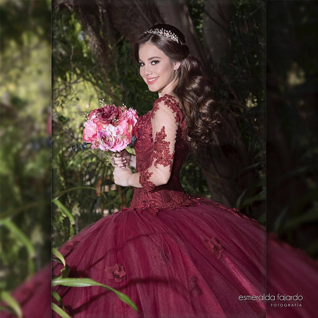 A beautiful Quinceañera wearing a red gown and holding a bouquet of flowers
