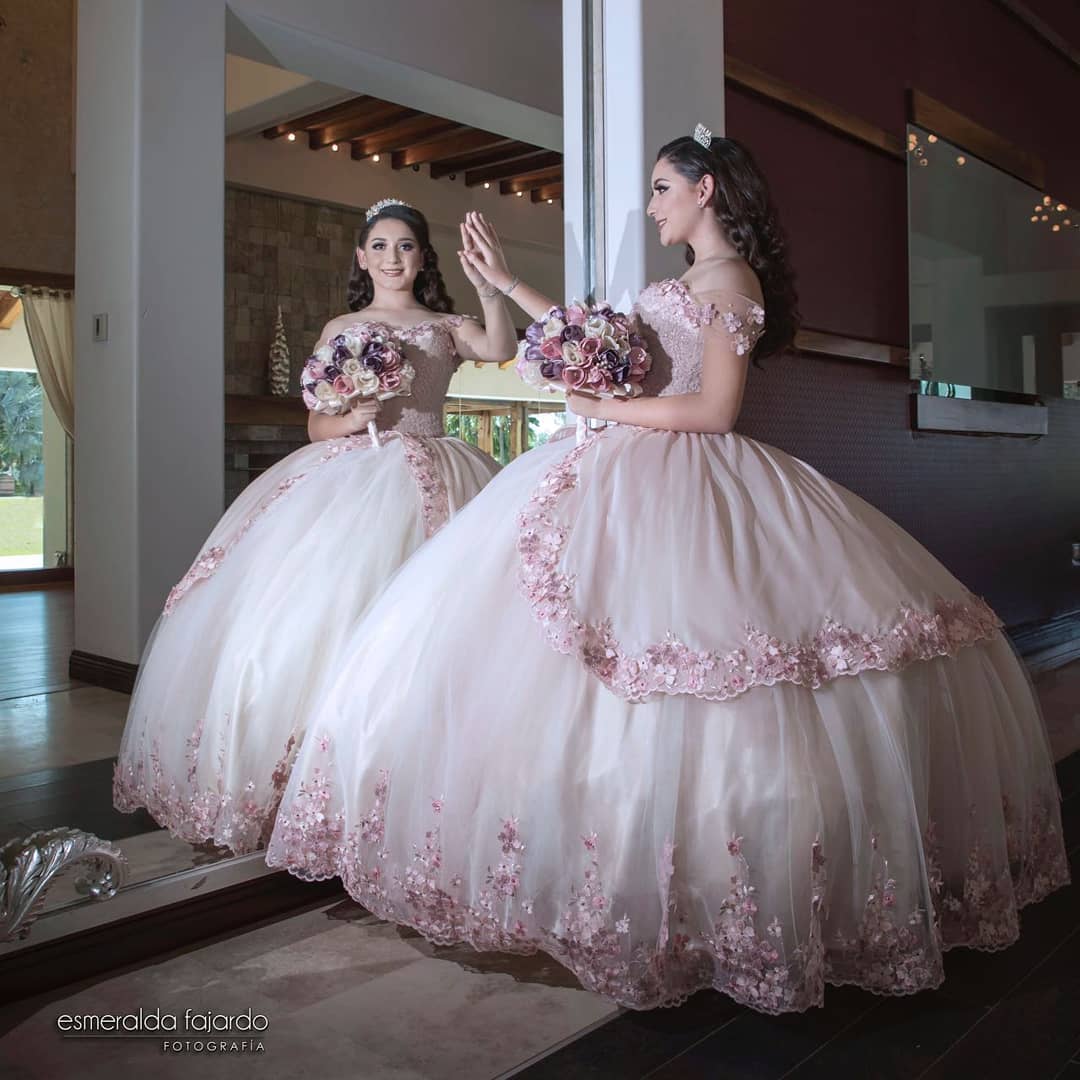 Two quinceanera dresses on display, one is a ball gown and two women are standing in front of a mirror