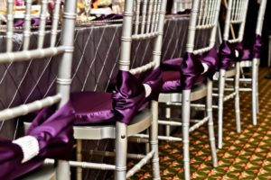 A row of chairs covered in purple ribbons, set up for a Quinceanera celebration