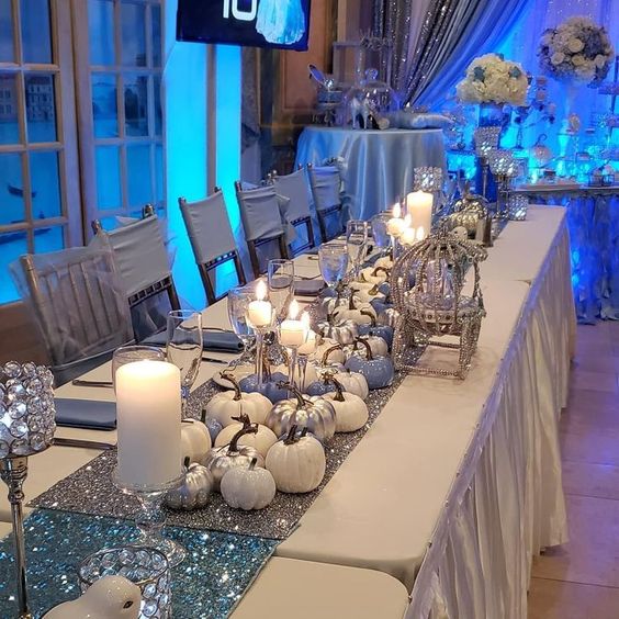 A Quinceanera image featuring a Cinderella themed sweet sixteen party. The image displays a long table adorned with silver and white decorations.
