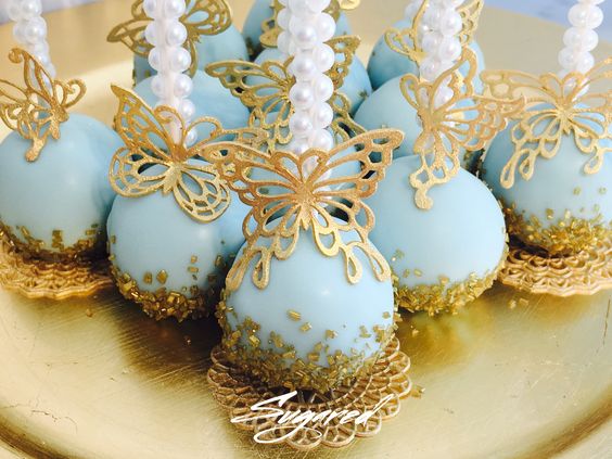 A Quinceanera-themed image featuring a chocolate cake on a gold plate topped with blue and white cake pops.