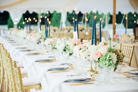 A Quinceanera celebration with a floral design at a function hall. The long table is filled with plates and candles.