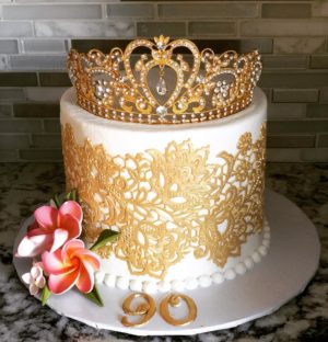 A Quinceanera cake with a pastel de encaje design, featuring a white and gold color scheme and a crown on top
