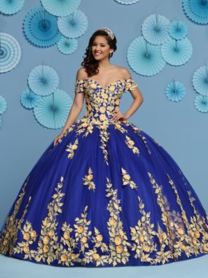 A woman in a blue and gold quinceanera dress, surrounded by other Quinceañera dresses