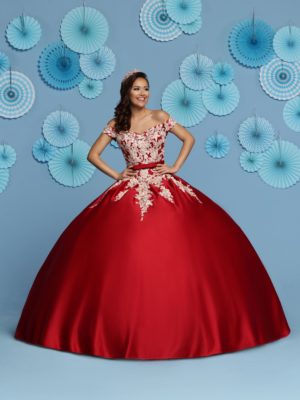 A woman in a red ball gown with a train, standing in front of fans. Quinceañera dresses
